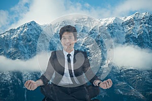 Businessman doing yoga position in front of snow-covered mountains