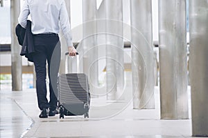 Businessman Dragging suitcase luggage,walking to passenger boarding in Airport.Asian tourist men wearing black suit with trolley