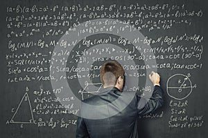 Businessman draws on concrete wall of the mathematical formulas. Business and education concept