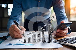 Businessman draws upward graph on paper holding pen and smartphone, showcasing growth/profit