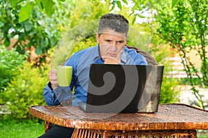 Businessman drinking coffee and reading news using laptop in his garden