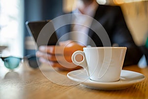 Businessman drinking morning coffee from big white cup and reading news on mobile phone