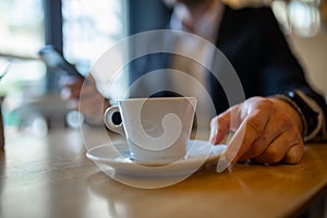 Businessman drinking morning coffee from big white cup and reading news on mobile phone