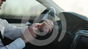 Businessman driving car at sunset. Man watch notification. Close-up driver hands at steering wheel wearing modern smart