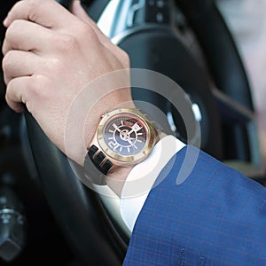 Businessman driving his car, hand on the steering wheel. Hand with golden watch. Business concept