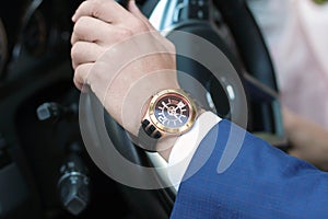 Businessman driving his car, hand on the steering wheel. Hand with golden watch.ness concept.