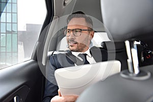 Businessman driving in taxi using tablet