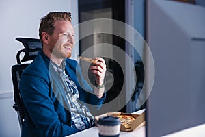 Businessman eating pizza and drinking coffee while working late in an office