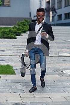 Businessman with electric scooter walking in front of modern business building looking at phone.