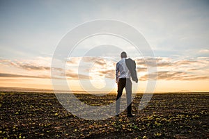 Businessman in elegant suit with his jacket hanging in field