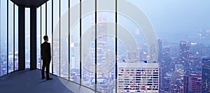 Businessman in empty office looking out of panoramic window with bright city downtown and sky view with mock up place. Future,