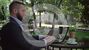Businessman ends work after reading bad news on laptop, outdoor. Steadicam shot.
