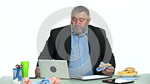 Businessman enjoying burger while sitting at desktop at office.