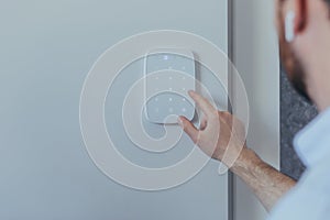 Businessman enters finger password lock code on alarm panel, on white wall, rear view of man with beard