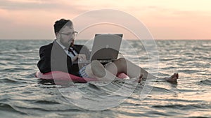 Businessman enthusiastically working at a laptop swaying on the waves of a reservoir and sitting on a children`s