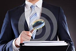 Businessman examining documents with magnifying glass