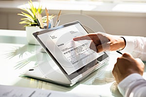 Businessman examining invoice on laptop