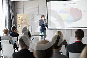 Businessman explaining pie chart to audience in seminar hall