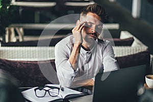 Businessman feeling headache while doing distance work in coffee shop tired with failure of plans, male entrepreneur