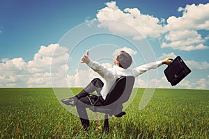 businessman in a field with a blue sky sitting on an office chair and waving his arms