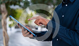 Businessman finger touch tablet on blurred park background, closeup