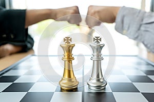 Businessman fist bump  near the chess board silver and gold color on the office desk