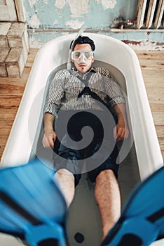 Businessman in flippers and mask lies in bathtub