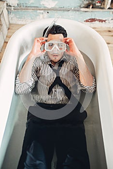 Businessman in flippers and mask lies in bathtub