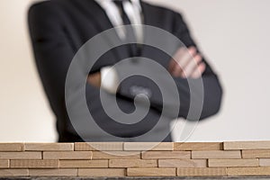 Businessman with folded arms with wall of wooden bricks infront