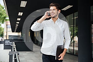 Businessman with folder talking on cell phone near business center