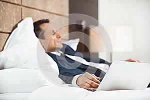 Businessman in formal suit falling asleep on bed in hotel room