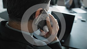 Businessman in full suit is sitting at the office desk at the meeting and talking on the phone. Talking business details