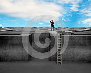 Businessman gazing on top of concrete Maze wall with ladder