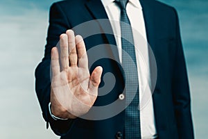 Businessman gesture. Male palm close-up in a gesture of stop. In the background a man in a blue suit with a tie