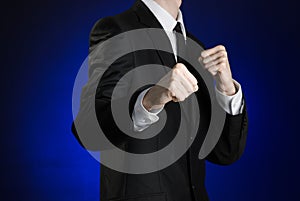 Businessman and gesture topic: a man in a black suit and white shirt holding his fists in front of him on a dark blue background
