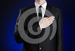 Businessman and gesture topic: a man in a black suit and white shirt, put his hand on his chest on a dark blue background in