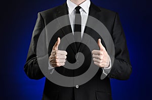 Businessman and gesture topic: a man in a black suit and white shirt showing hand gestures a thumbs-up on a dark blue background