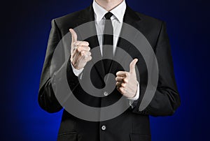 Businessman and gesture topic: a man in a black suit and white shirt showing hand gestures a thumbs-up on a dark blue background