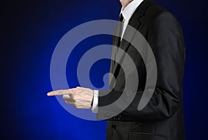 Businessman and gesture topic: a man in a black suit and white shirt shows his hand forward on a dark blue background in studio is