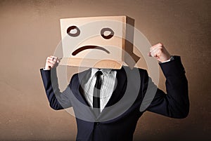 Businessman gesturing with cardboard box on his head with sad fa
