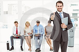 Businessman gesturing thumbs up against people waiting for interview