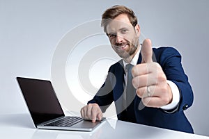 Businessman giving a thumbs up and working on his laptop