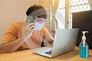 Businessman with glasses in casual dress talking by mobile phone, working on laptop computers at home, idea for coronavirus crisis