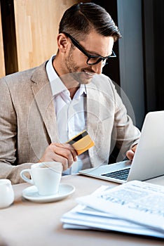 Businessman in glasses with credit card and laptop in cafe