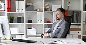 Businessman in gray jacket sitting at table in white office, looking at clock and leaving on office-chair