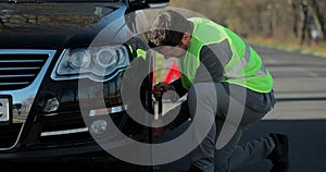 Businessman in a green safety vest changes a flat tire on a road. Mans hands to the wheel of a broken car. Concept road