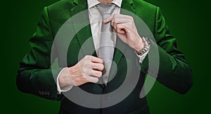 Businessman in green suit tying necktie, on dark green background. Environmental and agriculture business