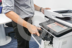 Businessman in grey shirt put ink toner cartridge into office multifunction printer for printing documents