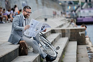 businessman in grey suit reading newspaper on stairs