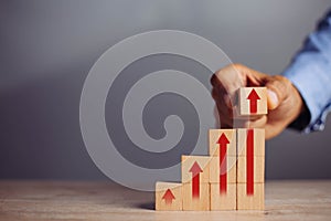 Businessman hand  arranging wood block stacking as step stair with arrow up.concept for business growth success process